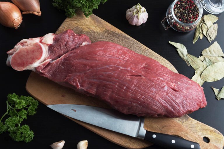 Raw,Beef,Shoulder,On,A,Cutting,Board,,Next,To,Greens